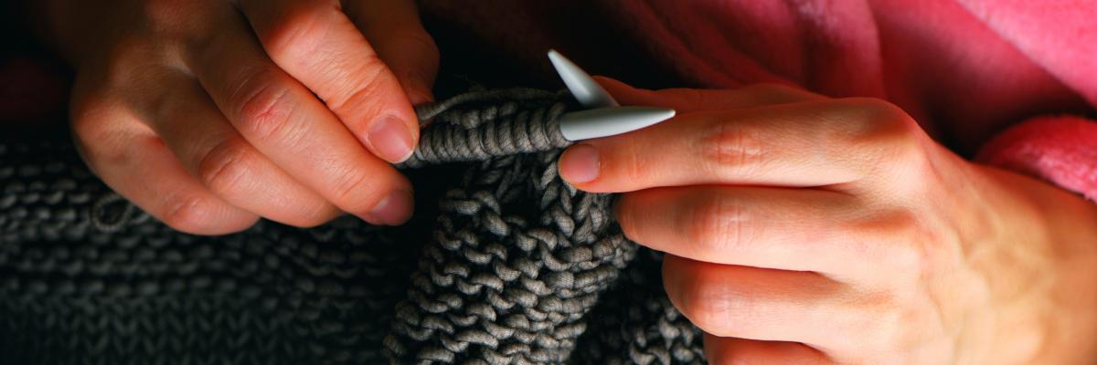 Hands holding knitting needles with partially knitted item.