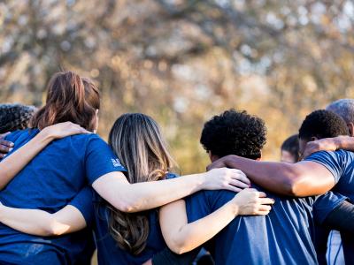A group of four volunteers in matching navy shirts with their arms around each other