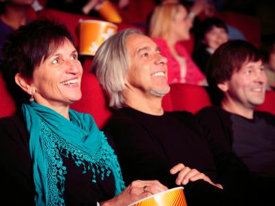Adults sitting in red cinema seats, looking up at the screen to watch a film or movie.