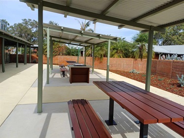 Courtyard showing three picnic seats under shelter with barbecue in between