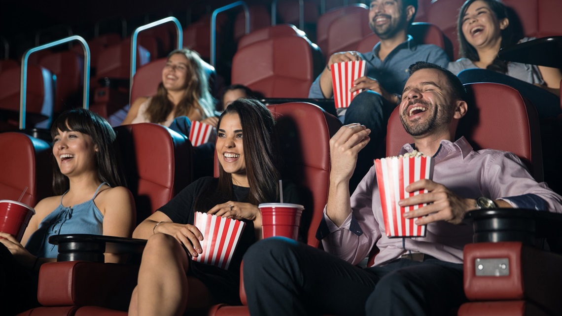 People sitting in red cinema seats eating popcorn and watching the film