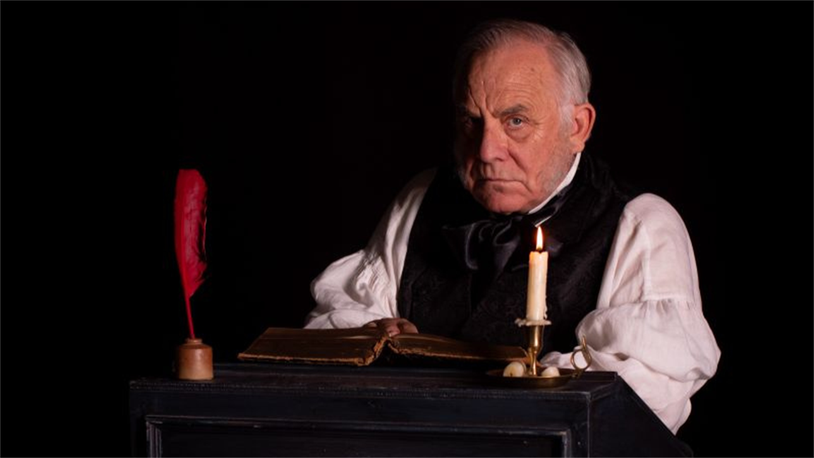 Ebenezer Scrooge sitting at a writing desk.