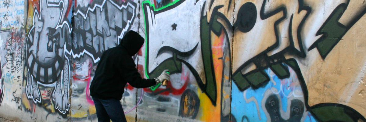 Man outlining a tag with spray paint on a public wall