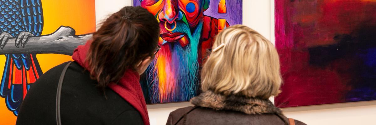 Two women viewing a bright and vivid artwork at the Community Art Exhibition and Awards 2021