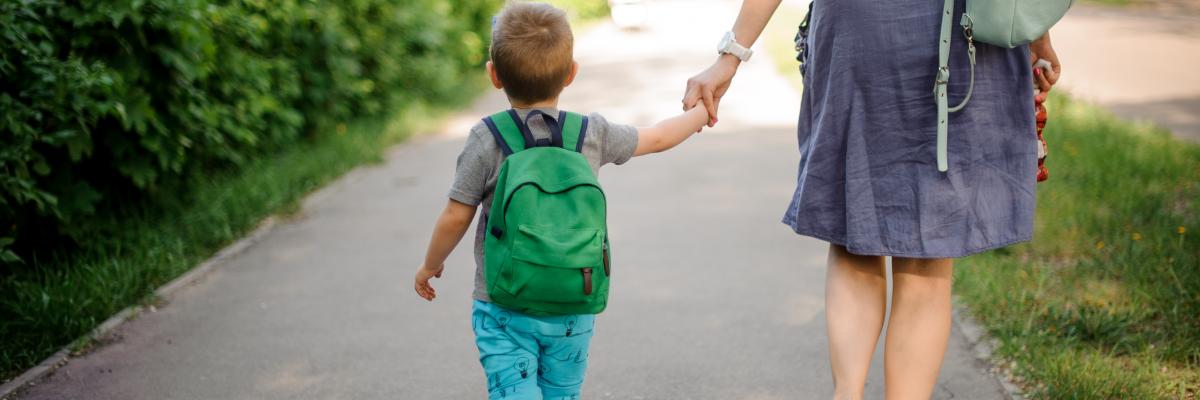 Child and parent hold hands while walking along footpath
