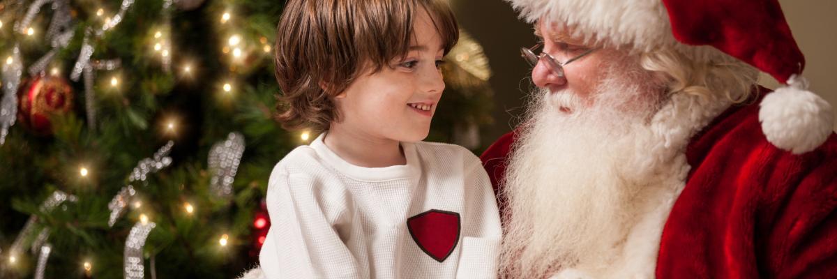 Child sits on Santa Claus' lap in front of a Christmas tree
