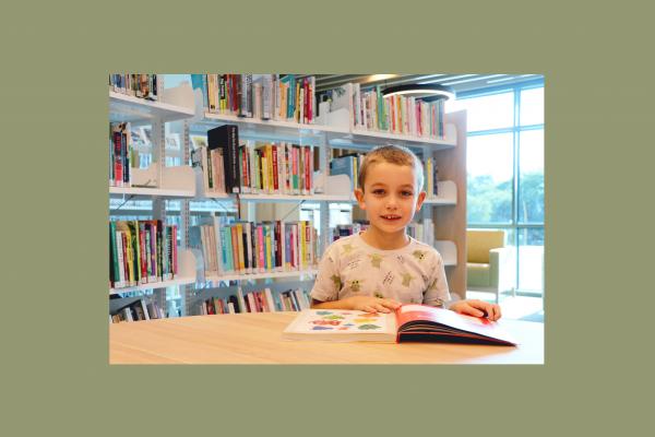 young boy reading in front of book shelves