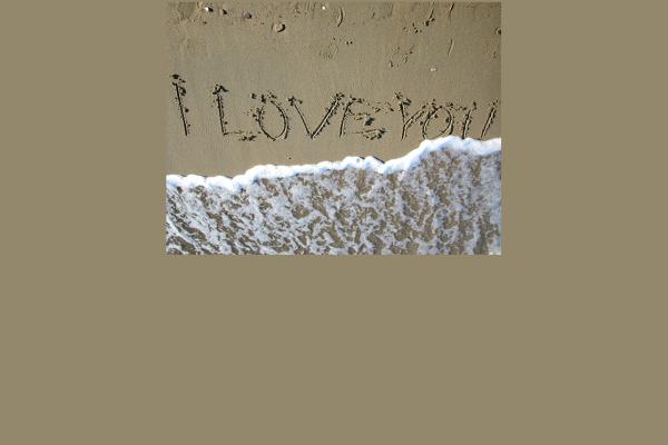 I love you scratched into beach sand with a wave almost wiping it out