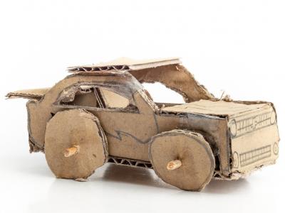 Small toy car made from brown cardboard, wheels attached with skewers.