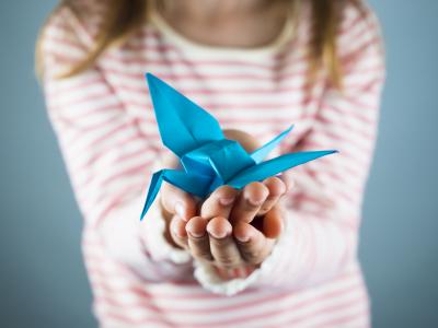 Young girl (face obscured) holding a blue origami crane
