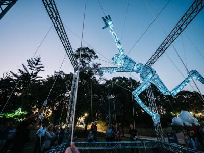 The String Symphony puppet reaching out and illuminated against a dusk sky