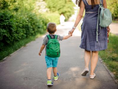 Child and parent hold hands while walking along footpath