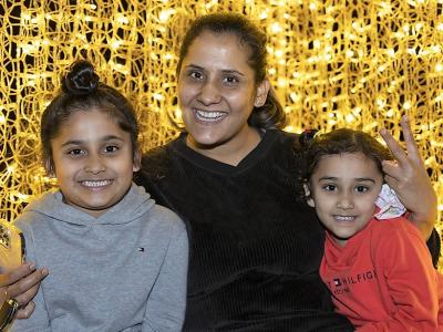 Mother and two children smiling in front of golden Christmas lights