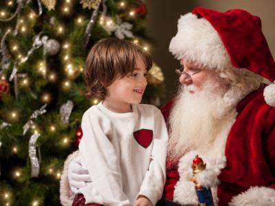 Child sits on Santa Claus' lap in front of a Christmas tree