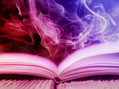 Open book lying flat on table with smoke and coloured lighting above to create a mystical feeling.
