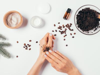 Hand rubbing a coffee scrub into other hand, with various bowls of ingredients scattered around a table.